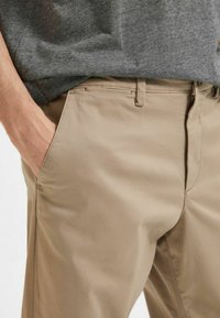 Beige chinos med en slät textur, med flat kant, bältesöglor och sidofickor. Parat med en grå T-shirt.