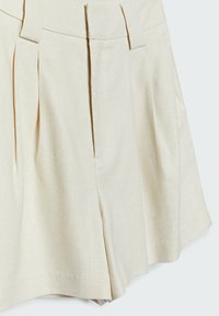 Jupe plissée beige en tissu texturé, dotée d'une taille ajustée et de poches latérales, avec un ourlet évasé.