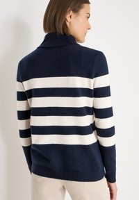 Pull rayé bleu marine et crème avec un col montant et un ourlet côtelé, doté d'une texture tricotée confortable et d'une coupe décontractée.
