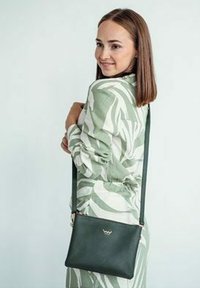 Zelená kožená crossbody taška s minimalistickým designem, se zlatým logem jako akcentem. Hladký povrch, nastavitelné ucho a obdélníkový tvar.