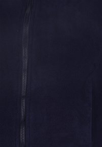 Giacca in pile blu navy con texture liscia, chiusura verticale con cerniera e cuciture piatte. Il materiale è morbido con una finitura leggermente pelosa.