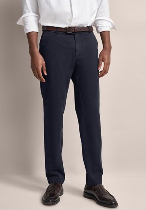 Navy chinos made of cotton, featuring a straight leg design, front button closure, and classic belt loops. Paired with a brown belt.