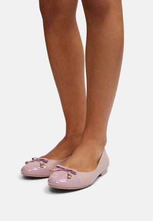 Ben klædt i lyserøde ballerinaer med kviltede, skinnende tåkapper og små sløjfer med gyldne accenter på en ensfarvet hvid baggrund.