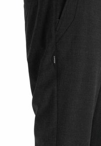 Schwarze karierte Hose mit strukturiertem Stoff und glatter Oberfläche, Seitentaschen und kleinem Markenzeichen an der Seitennaht.