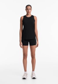 Sort atletisk tanktop og shorts, letvægtsstof, ærmeløs design, minimalistisk stil, parret med hvide sneakers.