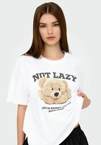 White oversized t-shirt featuring a soft, plush teddy bear graphic, with the text “NOT LAZY” in bold black above and a caption below.