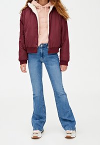 Bordeaux bomberjakke med pelskrave, parret med en pink hættebluse og lyseblå flare jeans. Hvide sneakers med detaljer afslutter looket.