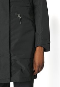 Giacca impermeabile nera con tasca sul petto con cerniera, tessuto testurizzato e polsini regolabili. Il design è pratico e moderno.