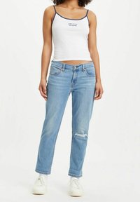 Camiseta sin mangas blanca con ribetes azul marino, combinada con jeans de mezclilla azul claro que presentan una rodilla desgastada, corte recto y diseño clásico de cinco bolsillos.