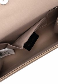 Sisäinen vaaleanbeige laukku, jossa on sileä satiinimainen kangas. Varustettu mustalla merkillä, korttitaskulla ja hopeisella nipistyskiinnityksellä. Ei näkyviä kuvioita.