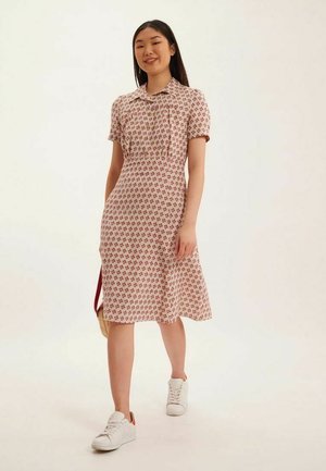 Robe à manches courtes, rose pâle avec un motif floral rouge, col, et ourlet évasé. Associée à des baskets blanches pour un look décontracté.