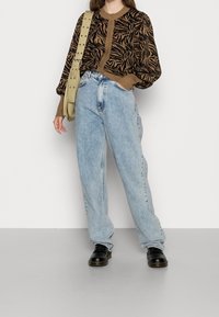 Brun och svart zebra-mönstrad tröja, lösa ljusblå jeans, svarta snörskor, beige väska med nitar. Slät tygtextur, avslappnad passform.