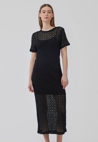 Abito nero in pizzo con un motivo a zig-zag texturizzato, maniche corte e orlo sopra il ginocchio. Materiale semitrasparente con una silhouette aderente.