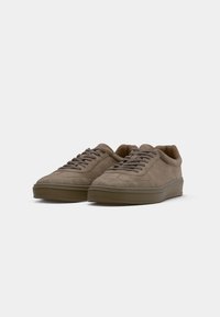 Paire de baskets basses en daim taupe avec lacets et semelles en caoutchouc sur un fond clair uni.