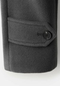 Manica di un cappotto di lana grigio scuro con una tasca cucita, caratterizzata da una forma arrotondata e un bottone nero con un design visibile a quattro fori.