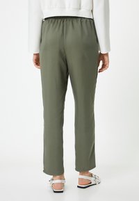 Olive green jogger pants o gładkiej, satynowej fakturze, z elastycznym paskiem w talii i luźnym krojem, w połączeniu z białymi sandałami.