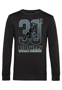 Sudadera negra con un gráfico de un personaje en una pose de acción, con "30 ANIVERSARIO" en una fuente estilizada y en negrita.