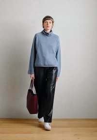 Svetlo modra pulover s turtleneck ovratnikom v kombinaciji s črnimi usnjenimi hlačami. Model nosi bordo torbo in bele superge. Gladke teksture.