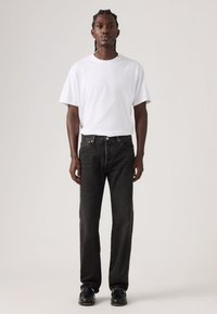 Μαύρα τζιν denim με ίσια γραμμή, εμπρόσθιες τσέπες και διακριτικά ράμματα. Συνδυασμένα με απλό λευκό κοντομάνικο μπλουζάκι και μαύρα παπούτσια.