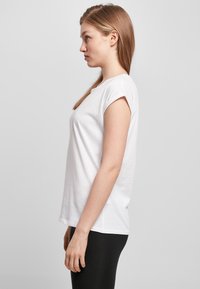 White cotton t-shirt with short sleeves and a rounded neckline, displayed from the side against a plain gray background.