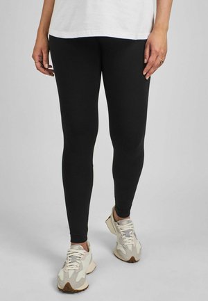 Mustad mustre ja sobiva lõikega mustad retuusid, millel on vähesed õmblused, koos heledate treeningjalatsitega, millel on tekstuuriga muster.