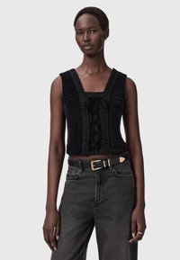 Czarna, krótka koszulka bez rękawów z aksamitnym wykończeniem i sznurówką z przodu, z teksturowanymi detalami na bandzie oraz szerokim dekoltem. Połączona z czarnymi jeansami z wysokim stanem.