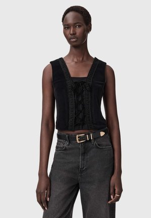 Czarna, krótka koszulka bez rękawów z aksamitnym wykończeniem i sznurówką z przodu, z teksturowanymi detalami na bandzie oraz szerokim dekoltem. Połączona z czarnymi jeansami z wysokim stanem.