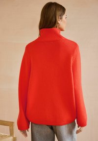 Czerwony sweter dziany z wysokim żebrowanym kołnierzem, opadającymi ramionami i szerokimi rękawami; charakteryzuje się luźnym krojem i teksturowanym materiałem.
