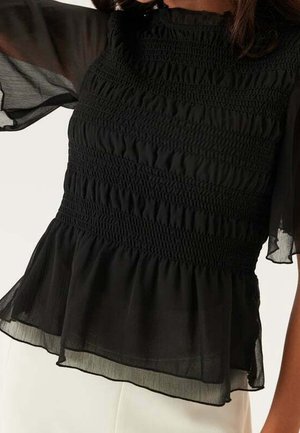 Zwarte blouse met gerimpeld lijfje, gerimpelde zoom en doorschijnende, zwierige mouwen, gedragen met een witte broek.