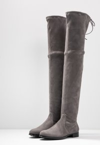 Botas grises por encima de la rodilla hechas de suave ante, con suela plana, punta redonda y parte superior ceñida con un lazo decorativo.