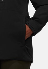 Schwarze wasserdichte Jacke mit Reißverschlusstaschen, glatter Textur und strukturiertem Design, mit einem umgeschlagenen Ärmel, der einen Arm zeigt.