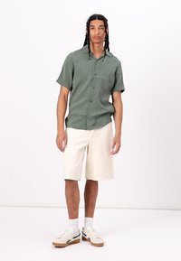 Light green short-sleeve button-up shirt with a smooth texture, paired with cream-colored knee-length shorts and cream sneakers with black accents.