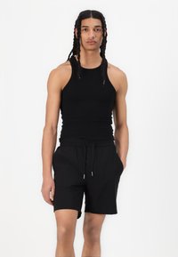 Canotta nera senza maniche abbinata a pantaloni corti neri con coulisse, caratterizzati da una vestibilità comoda e tasche laterali, su uno sfondo bianco.