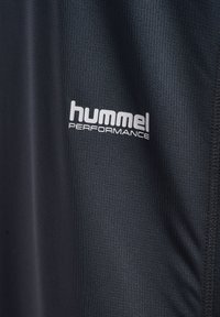 Czarna teksturowana tkanina z białym nadrukiem logo "hummel PERFORMANCE", pokazująca szczegóły tkaniny i szwy po prawej stronie.