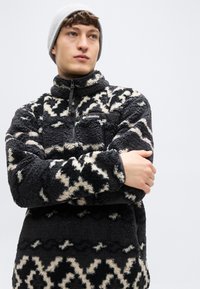 Μαύρο και κρεμ φλις πουλόβερ με μοτίβο, με γιακά με φερμουάρ και τσέπη στο στήθος με το λογότυπο της Columbia. Μαλακό, υφασμένο ύφασμα.