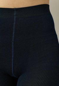 Granatowe legginsy w prążki z szerokim pasem, charakteryzujące się gładką teksturą i subtelnym detalem szwów wzdłuż środka przodu.