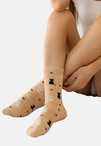 Kniestrümpfe in hellbrauner Farbe mit schwarzen Hundesilhouetten und kastanienbraunen Akzenten auf beigem Hintergrund. Weiches Baumwollmaterial.