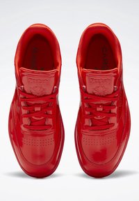 Para błyszczących czerwonych trampek Reebok Classic z sznurówkami, widok z góry na białym tle.