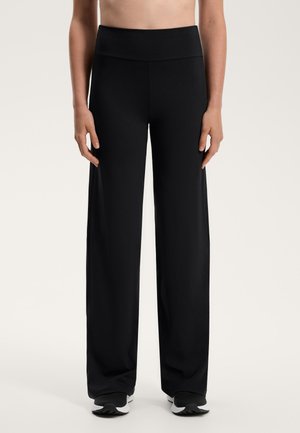 Schwarze weite Hosen mit hohem Bund, aus weichem, dehnbarem Stoff. Glatte Textur, minimales Design, kombiniert mit schwarzen Sportschuhen.