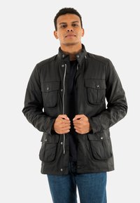 Zwarte, lichte jas met meerdere voorzakken, een ritssluiting en een hoge kraag. Gladde textuur en casual ontwerp.