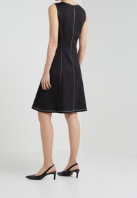 Abito nero senza maniche con gonna svasata, cuciture a contrasto e zip sul retro. Abbinato a tacchi a slingback neri.