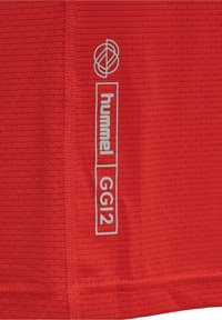 Červený sportovní dres s texturovaným povrchem, s šedým logem "hummel" a štítkem "GG12" na boku.