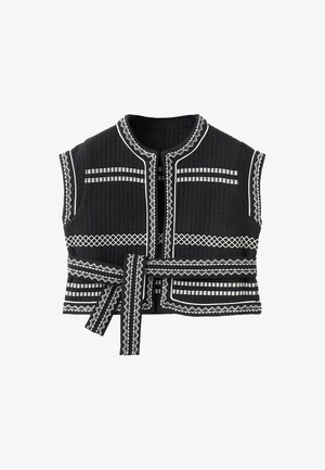 Musta tikattu liivi, jossa on valkoista geometrista brodeerausta, pyöreä pääntie, lyhyet hihat ja vyötetty vyötärö.