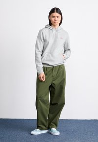 Grå hoodie med en frontlomme, olivengrønne baggy bukser og blå sneakers; glat tekstur og afslappet pasform, minimal branding på hoodien.
