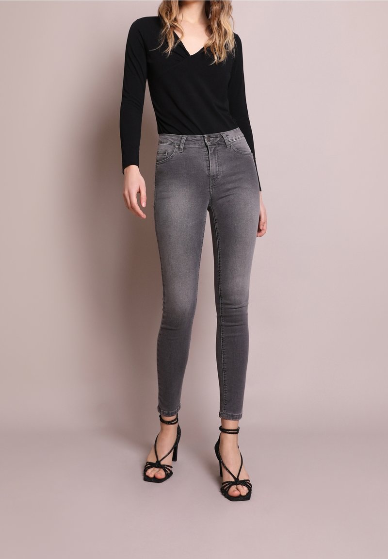 Body nero a maniche lunghe abbinato a jeans grigi aderenti. I jeans hanno una texture liscia e una vita alta, completati da tacchi neri con cinturini.