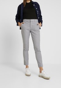 Kalhoty s kostkovaným vzorem v bílé a černé barvě, slim fit, se bočními kapsami. Spárováno s černým topem a námořnickým tílkem s knoflíky, a bílými teniskami.