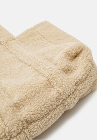 Beige fleecestof met een gestructureerd, zacht oppervlak. Heeft zichtbare stiksels en een iets puffy vorm, geschikt voor warmte en comfort.