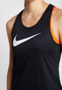 Top sportivo nero con logo Nike bianco. Presenta un colletto rotondo e audaci dettagli arancioni sulle spalline. Tessuto morbido e leggero.