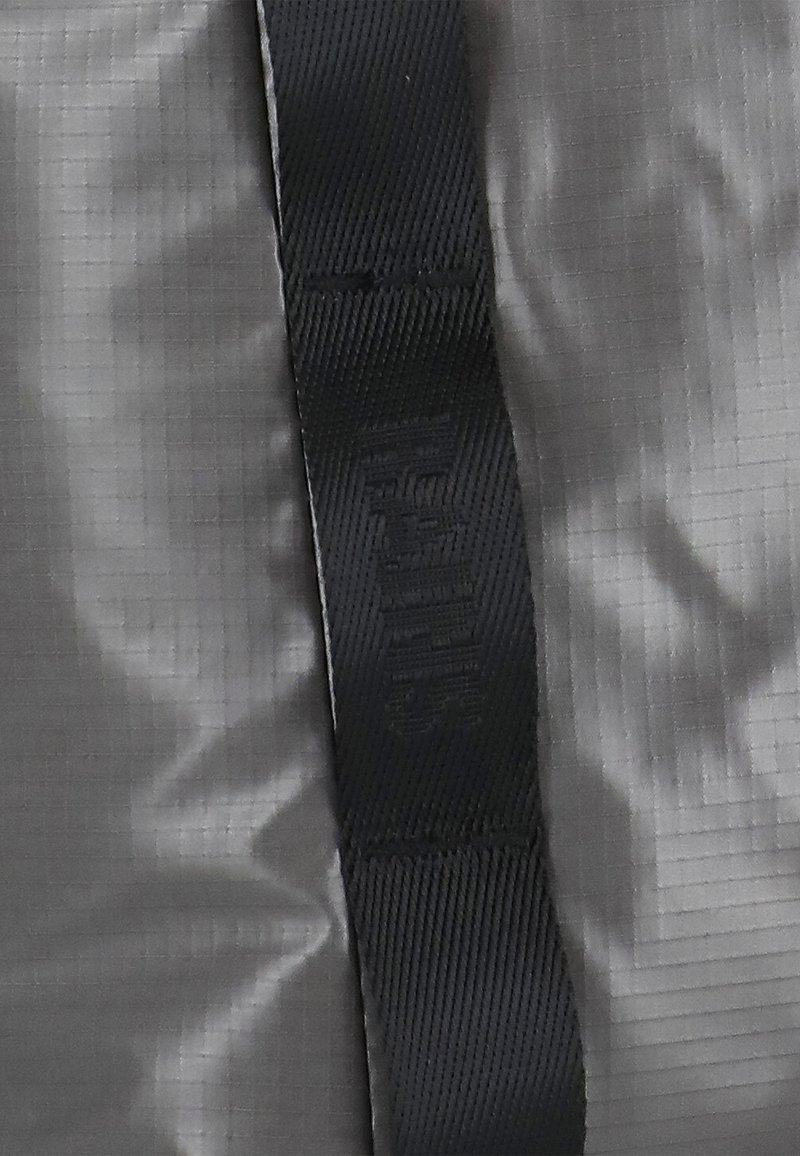 Szary materiał o lekko połyskującej powierzchni, z czarnym paskiem jako detalem. Tekstura jest gładka, z wzorem w kratkę oraz wytłoczonym logo na pasku.