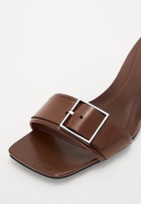 Sandale à talons hauts en cuir brun avec une large lanière, boucle rectangulaire en argent, bout carré et texture lisse.